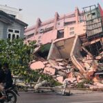 People drive on a motorbike past a collapsed building in Mandalay on March 28, 2025, after an earthquake in central Myanmar. Stringer/AFP/Getty Images