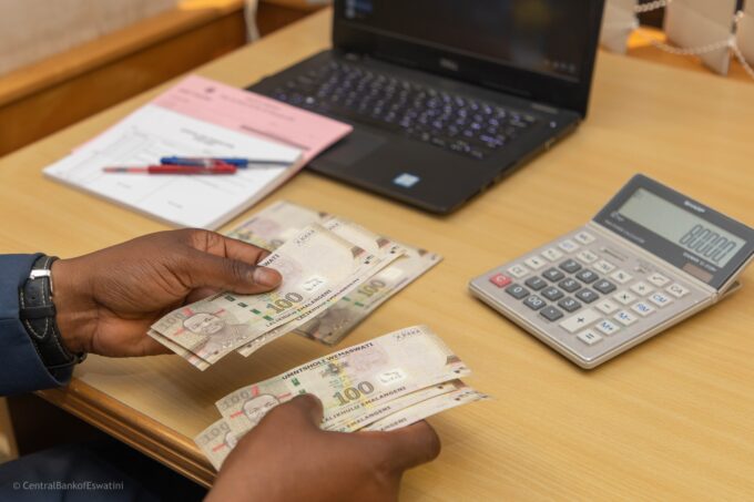 Photo of a hand holding Emalangeni banknotes with a calculator in the background,
