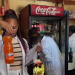 Health inspectors examine the expiry date on a bottled drink during a joint operation in Msunduza, while other officials inspect shelf items for compliance in the background. Photo: Municipal Council Of Mbabane
